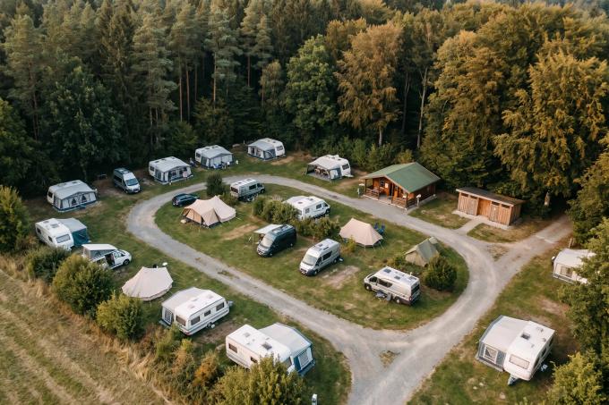 Luftbild eines kleinen Campingplatzes am Waldrand mit Wohnwagen, Zelten und Schotterwegen.